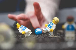 Une scène de Legographie représentant des lego qui jouent au foot contre une main. Au premier plan, des mini figures LEGO customisés au nom du club de foot de l’AOSP. La scène de cette legographie est réalisée sur un trottoir. Le ballon Lego est remplacé par une bille bleue.